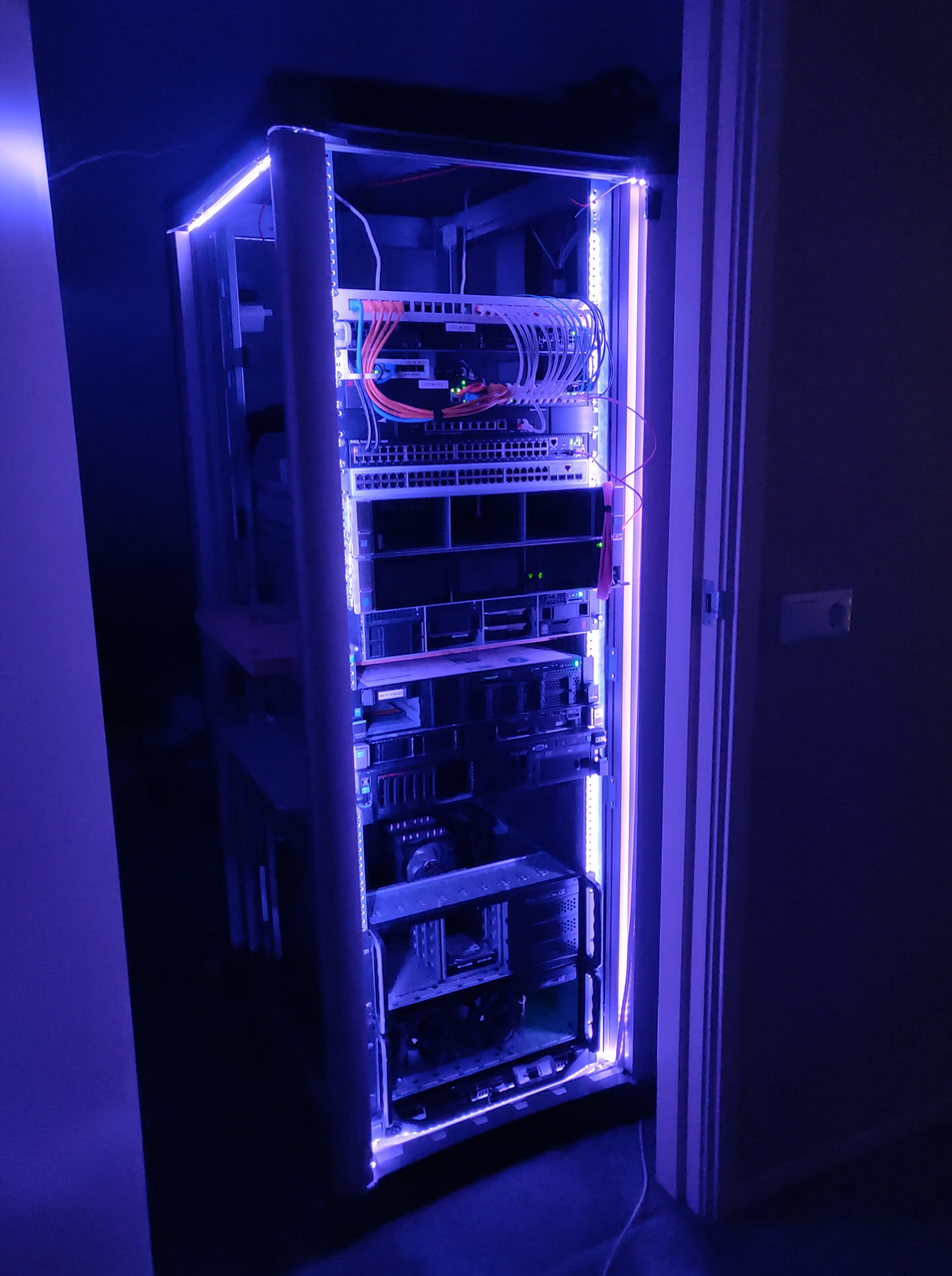 photograph of a server rack illuminated with purple led lights. it is about 40u, almost entirely filled with hardware. it looks very clean and not jank anymore